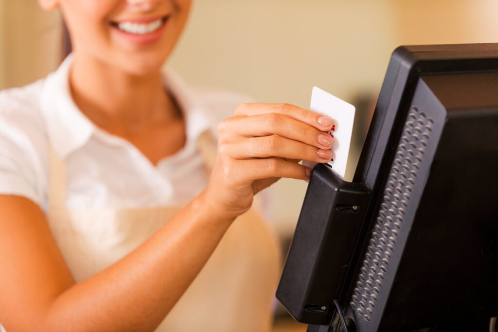 Cashier at work. Close-up of beautiful young female cashier swipes a plastic card through a machine