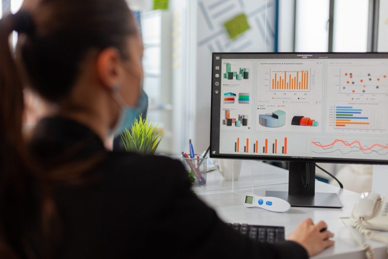 Businesswman analysing financial statistics in new normal offfice Businesswman analysing financial statistics in new normal offfice, wearing face mask as safety prevention during global pandemic with coronavirus flu, keeping social distancing.